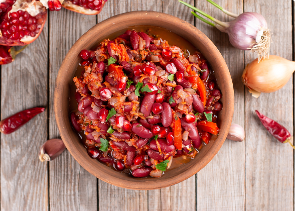 Tigela de barro com cozido de feijão vermelho decorado com romã e ervas.
