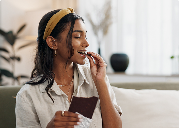 Mulher jovem com tiara amarela sorrindo ao morder um pedaço de chocolate.